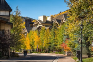 Vail Colorado in autumn fall golden yellow foliage aspen trees mountain peak with blue sky and hospital, unrecognizable people walking